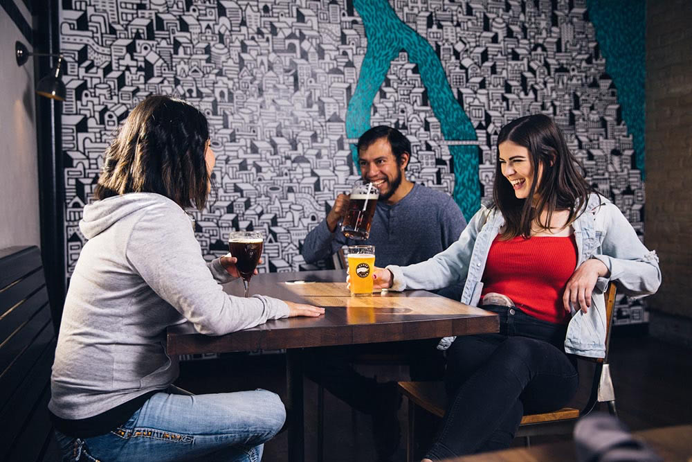 three smiling friends gathered round a table in a bar having drinks